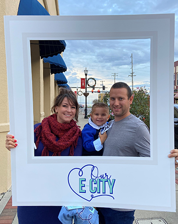 husband, wife, and toddler take selfie with Our E-City sign at ArtWalk in Elizabeth City NC